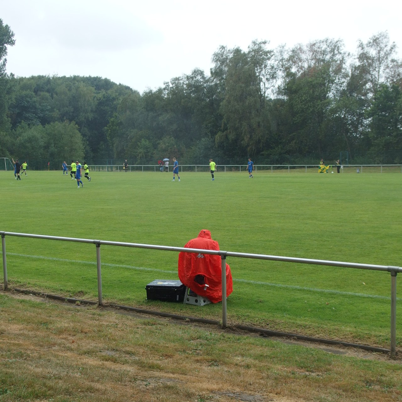 In rote Regenplane eingepackter Fotograf am Spielfeldrand beim Spiel FC 96 - Wacker Obercastrop In rote Regenplane eingepackter Fotograf am Spielfeldrand beim Spiel FC 96 - Wacker Obercastrop